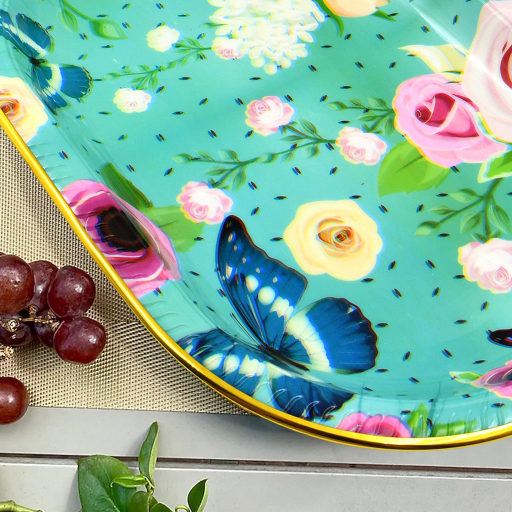 A close-up of the turquoise tray's floral and butterfly pattern, with a bunch of grapes in the foreground.