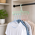 A light green multi-port hanger holds blue and pink hangers with various shirts in a closet.