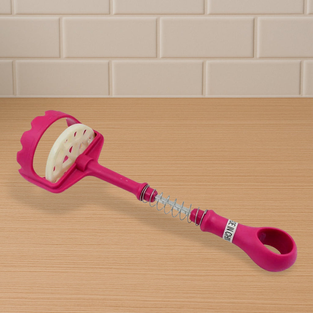 A pink and white plastic potato masher lies on a wooden surface, showing its spring mechanism.