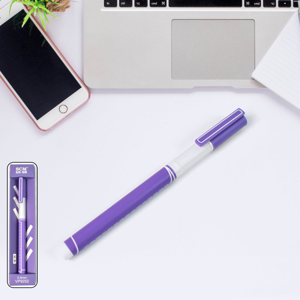 A purple gel pen with a white barrel lies on a white desk next to a phone and laptop