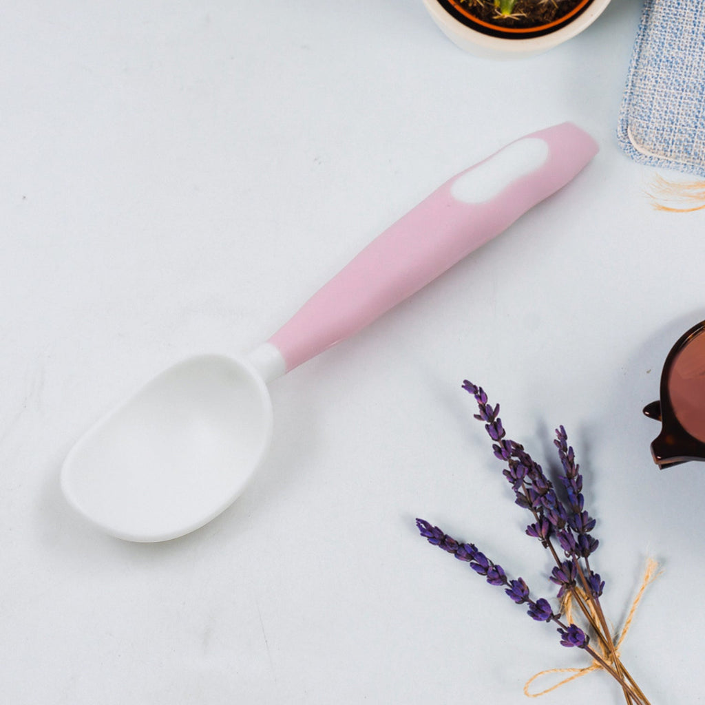 A pink and white baby spoon with a sprig of lavender and a brown object in the background.