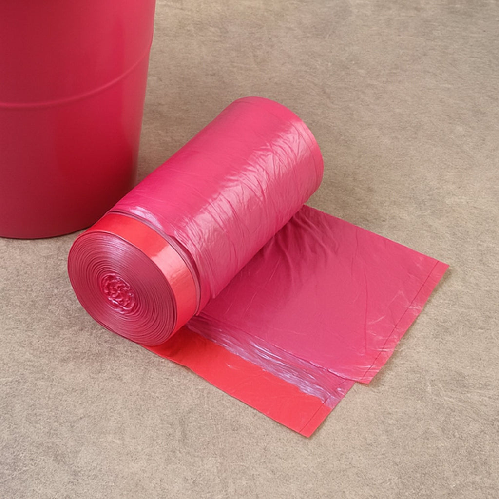 A roll of pink garbage bags with a red band sits on a brown surface next to a red bin.