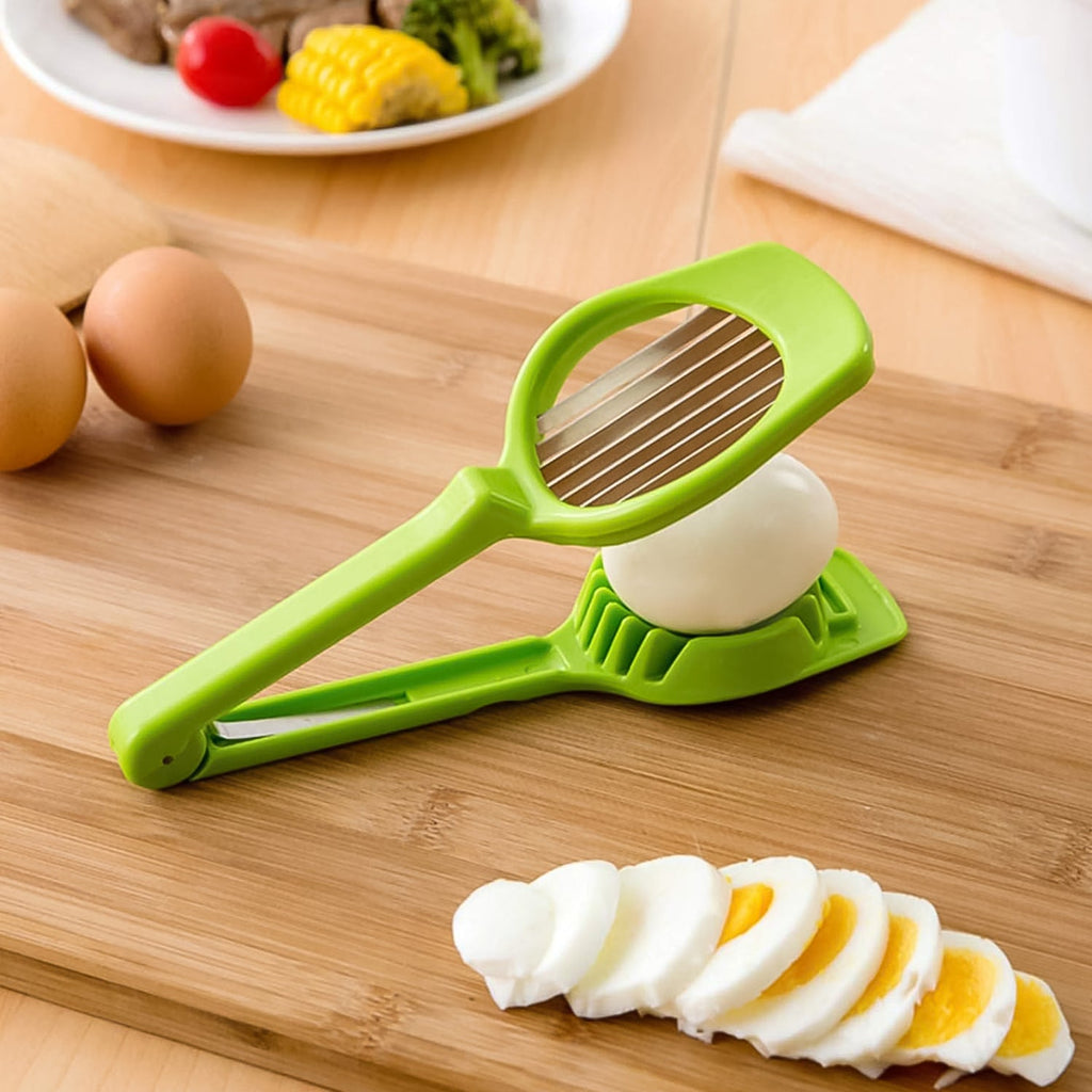 A green plastic slicer with metal blades rests on a wooden board next to a whole egg and perfectly sliced egg pieces.