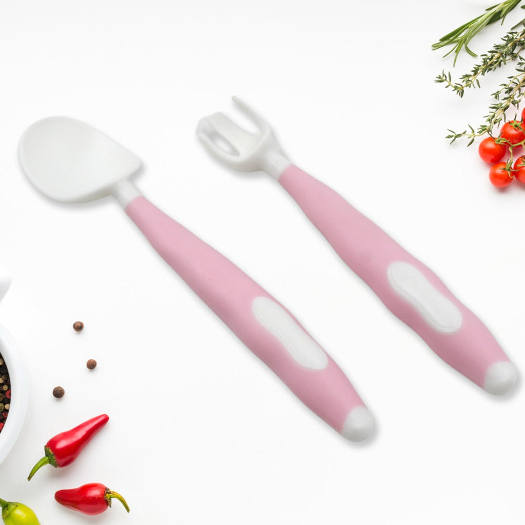 A pink and white baby spoon and fork set laid out on a white surface with small red peppers and spices.