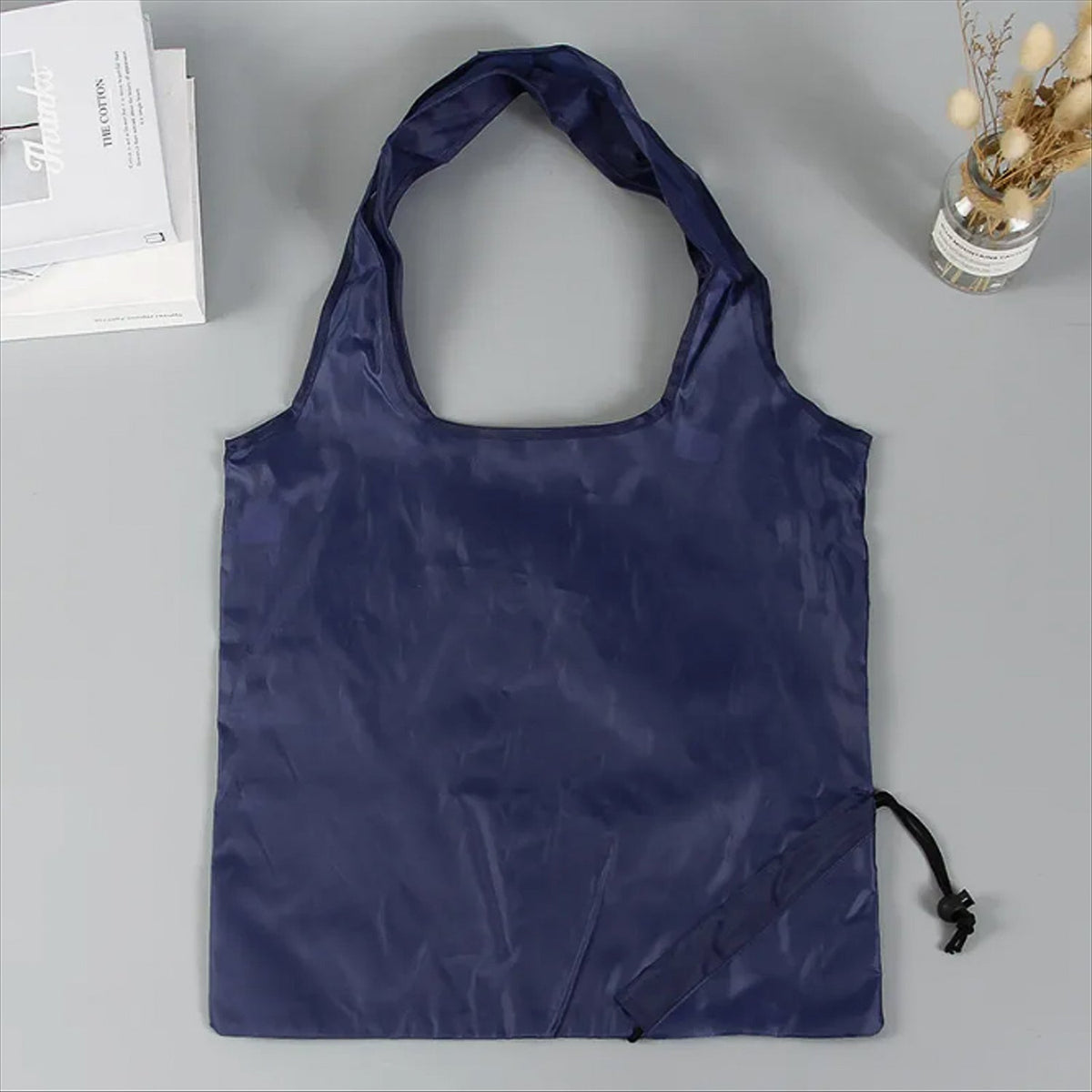 A dark blue reusable shopping bag with a drawstring pouch lies flat on a gray surface.