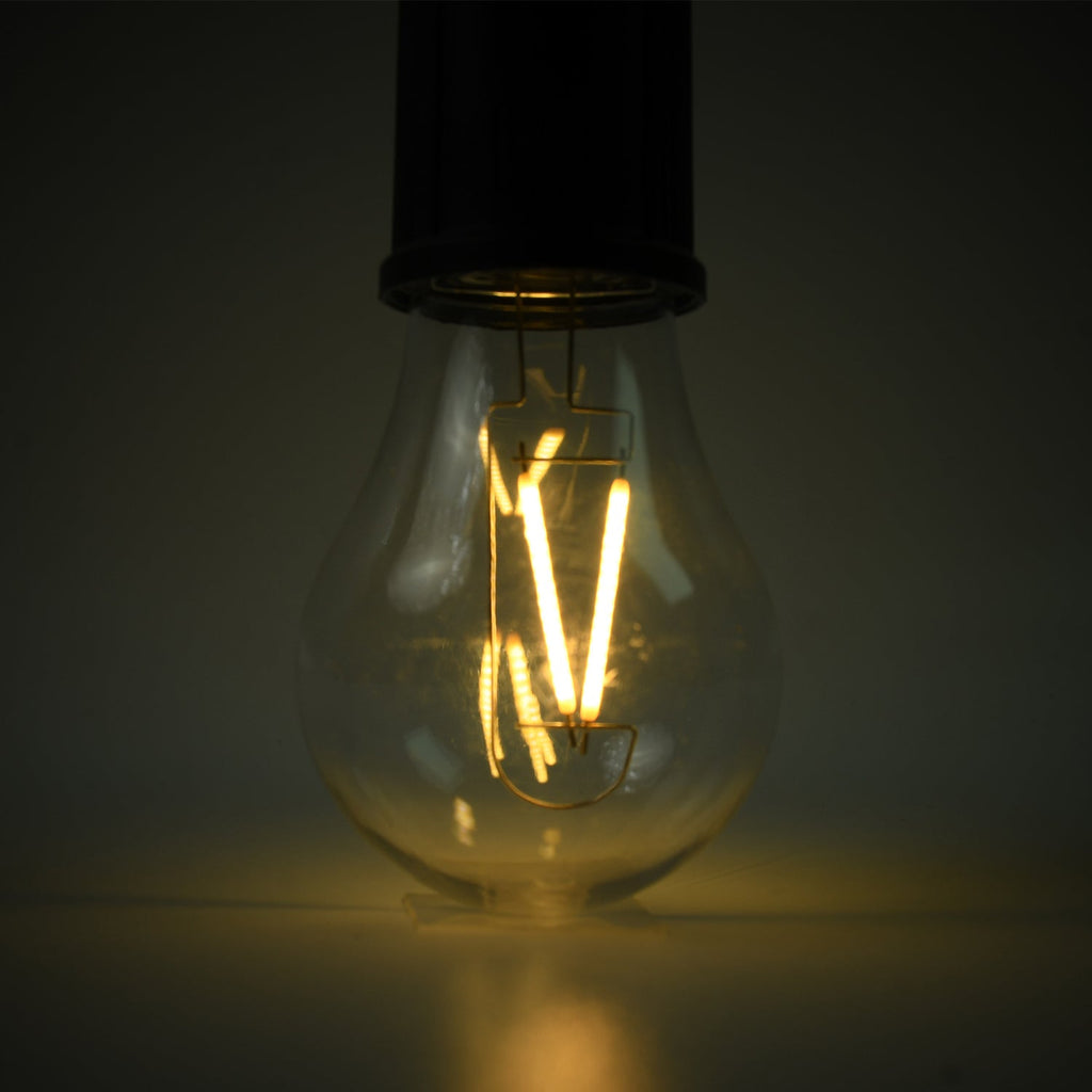 A close-up of the clear LED bulb shows its warm yellow filaments glowing brightly against a dark background.