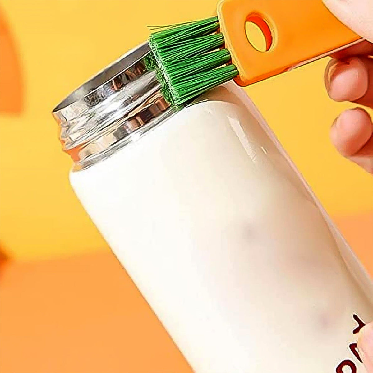 A close-up of the orange 3-in-1 brush with green bristles cleaning the rim of a white bottle.