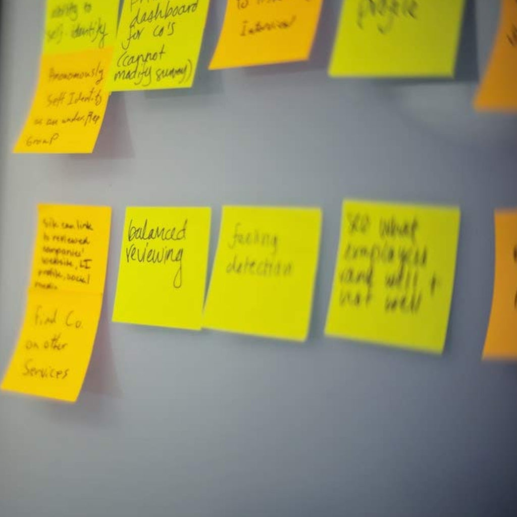A close-up of several yellow sticky notes with handwritten text, attached to a gray wall.