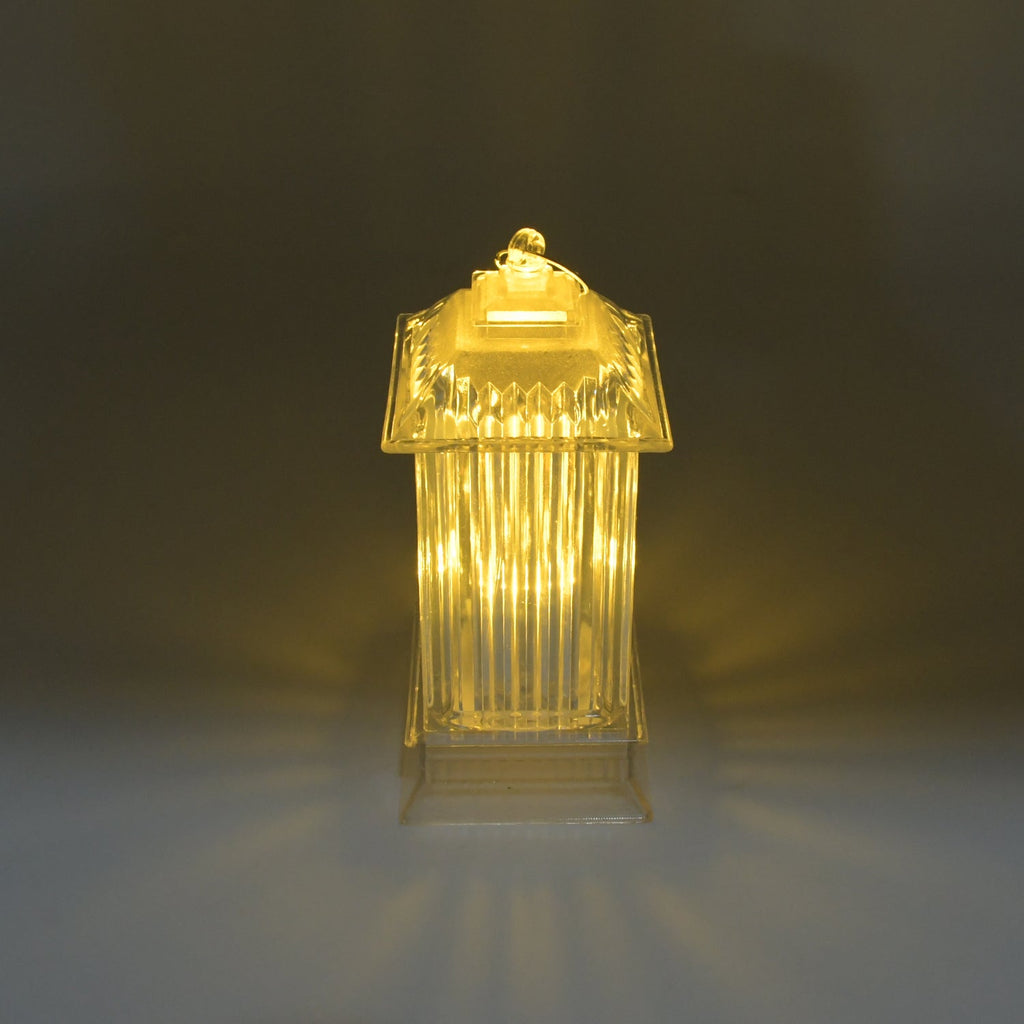 A single LED crystal lantern lamp emits a soft, warm glow on a subtly reflective surface in a dimly lit setting.