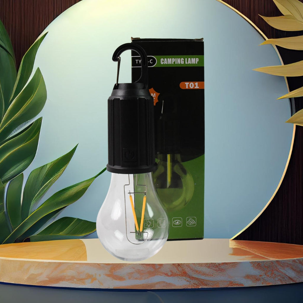 A clear LED bulb with a black top and hook stands on a marble pedestal, with its green and black packaging behind it.