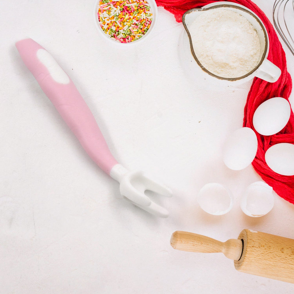 A pink and white baby fork with baking ingredients like eggs, flour, and sprinkles around it.