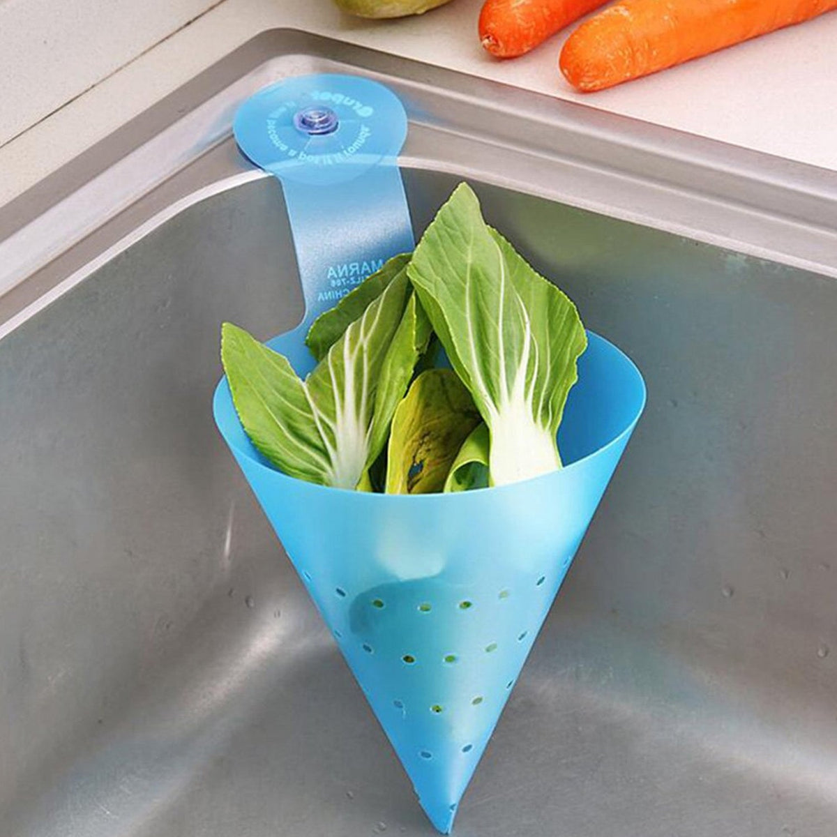 A blue silicone sink strainer with a suction cup, holding green leafy vegetables, attached to a metal sink.