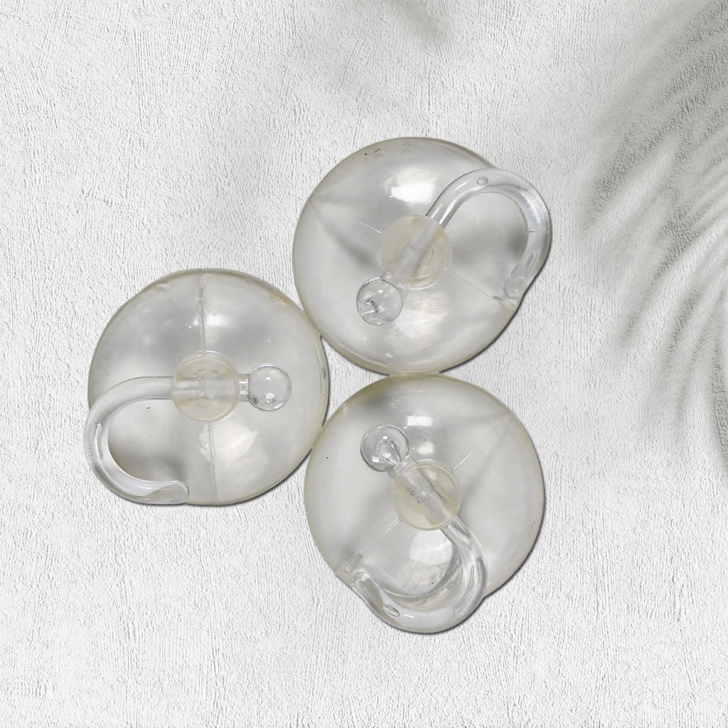 Three transparent suction cup hooks are arranged on a white textured surface with a subtle shadow.