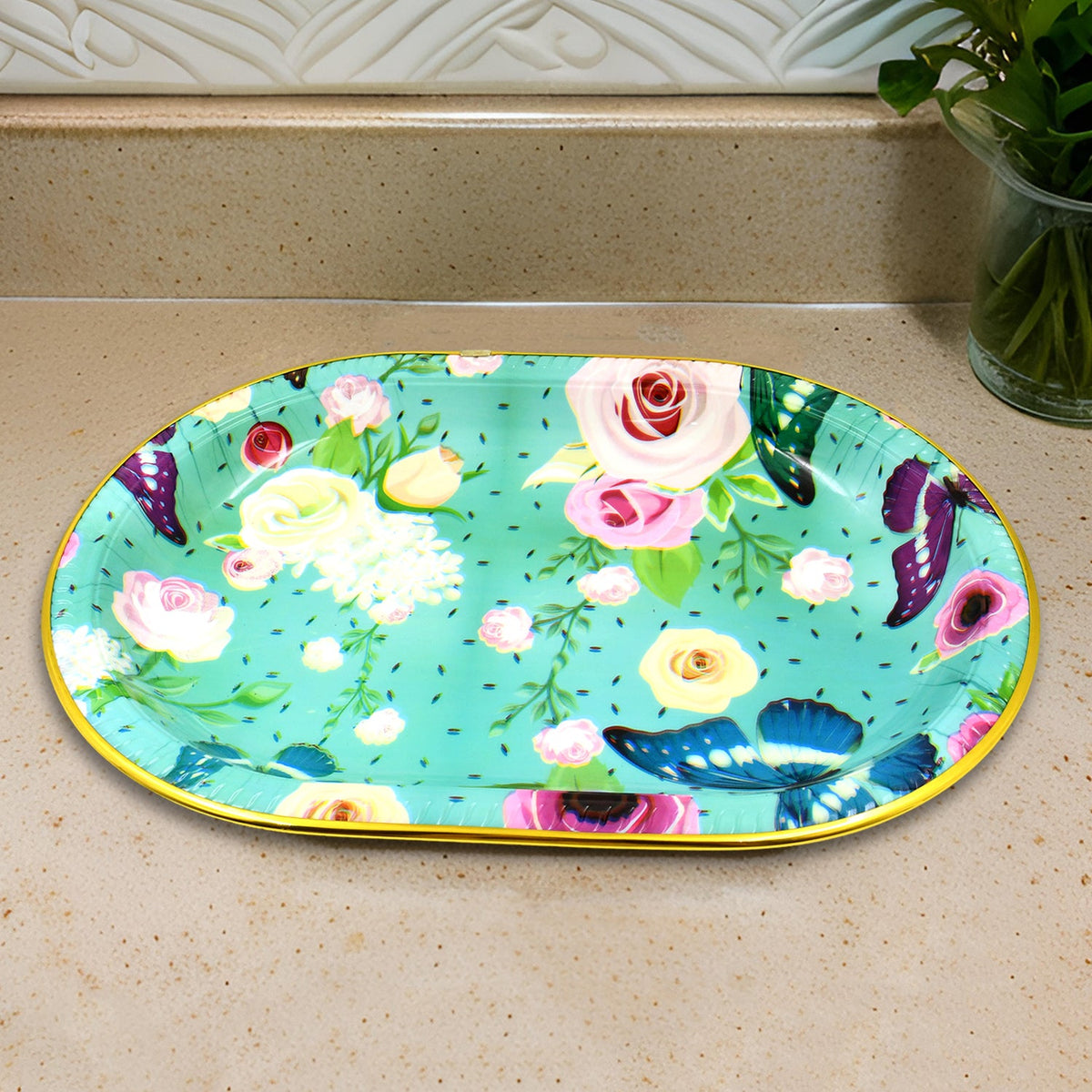 The oval turquoise tray with floral and butterfly print sits on a light brown countertop.