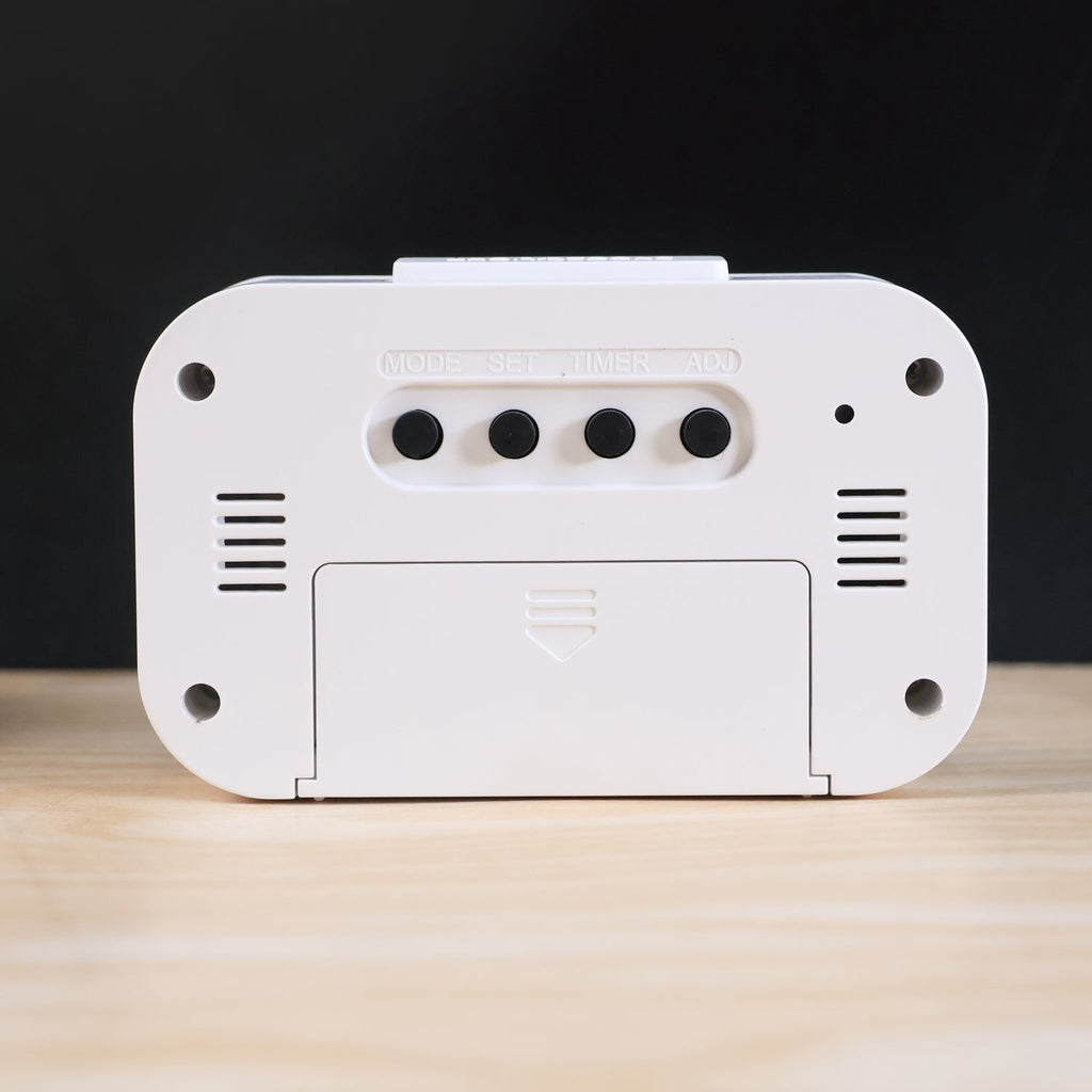 The back of a white digital clock reveals a battery cover and four black control buttons labeled MODE, SET, TIMER, ADJ.