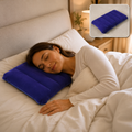 A woman with dark hair sleeps peacefully on a blue velvet inflatable pillow in a bed with white sheets.