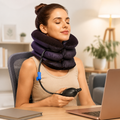 A woman with her eyes closed wears an inflatable neck traction device while sitting at a desk with a laptop.