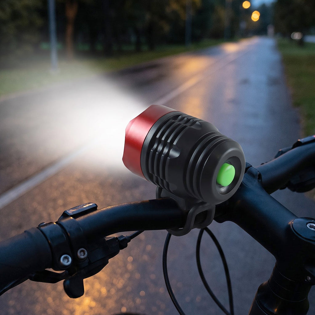 A red and black bicycle headlight with a green button illuminates a dark road from a bike's handlebars, with a small inset