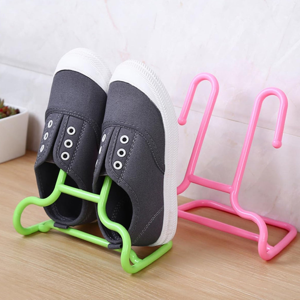 A pair of grey canvas shoes hangs from a green plastic drying rack next to a pink rack on a wooden surface.