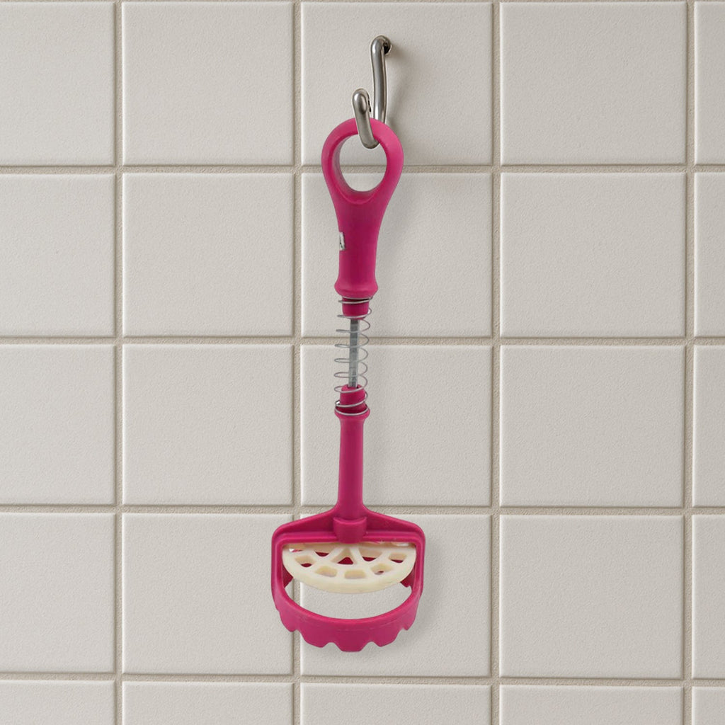 A pink and white plastic potato masher hangs vertically from a silver hook against a white tiled wall.