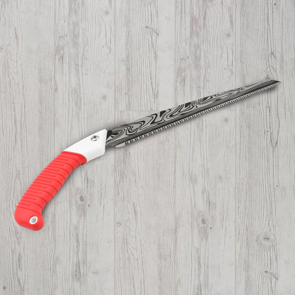 A hand pruning saw with a red handle and patterned blade lying diagonally on a light wooden floor.