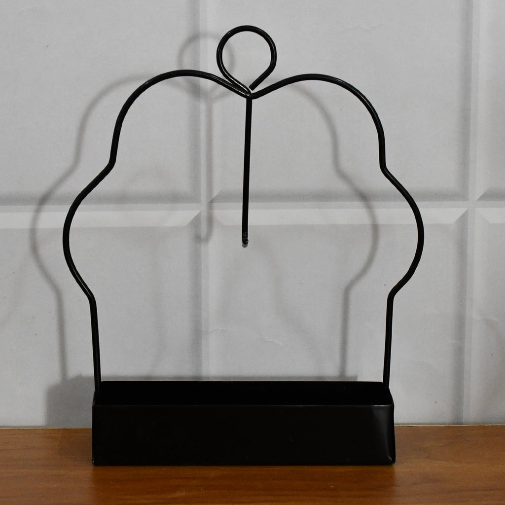A black metal mosquito coil holder with a rectangular base is positioned on a wooden surface against white tiles.