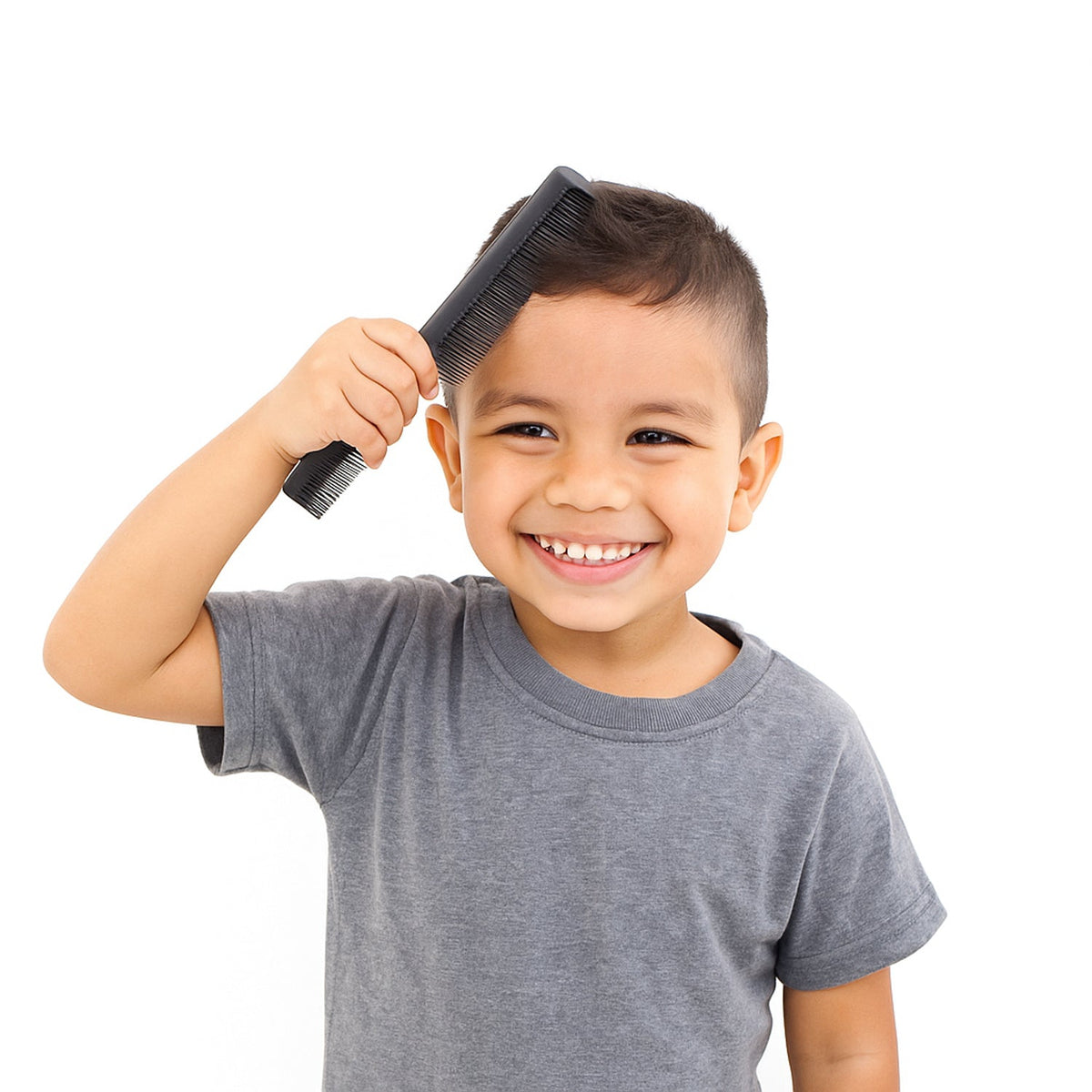 A young boy with short dark hair smiles while holding a black comb to his head.