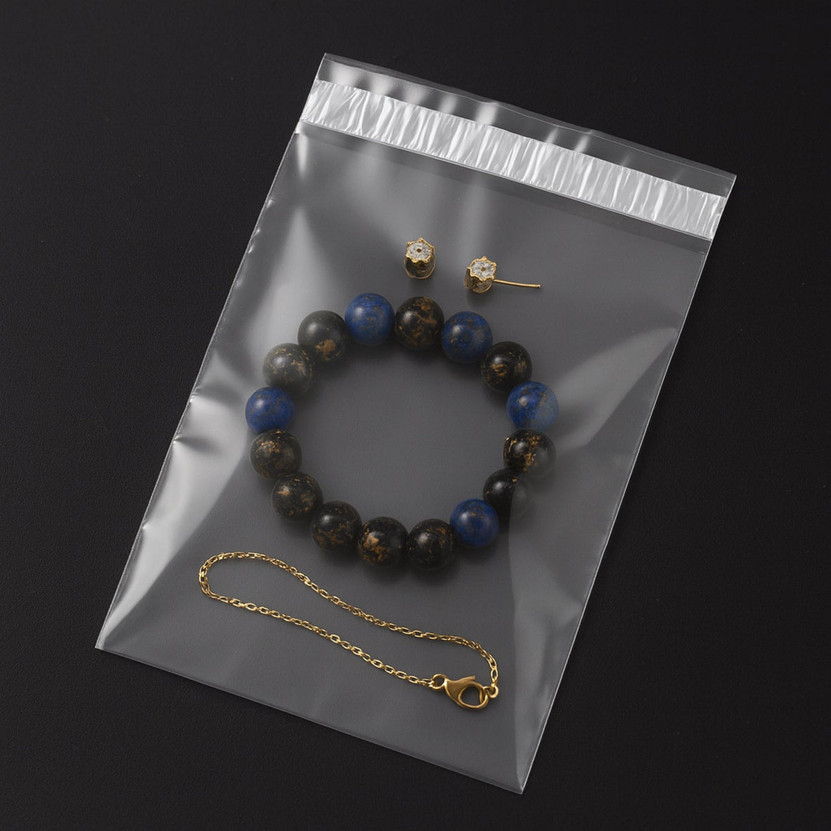 A clear polybag containing a blue and black beaded bracelet, a gold chain bracelet, and two small gold stud earrings.
