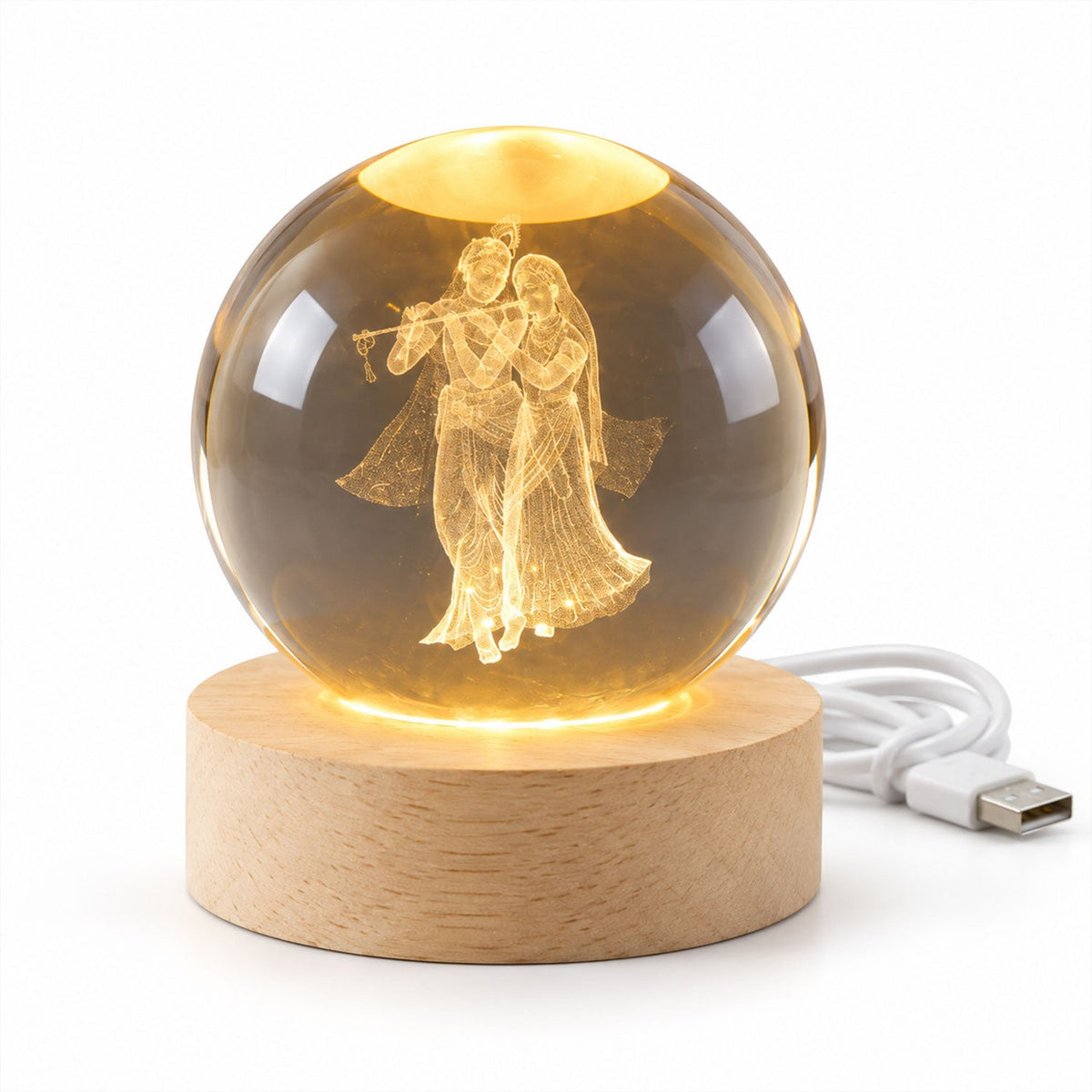 A glowing crystal ball with 3D Radha Krishna engraving on a light wooden base with a white USB cable.