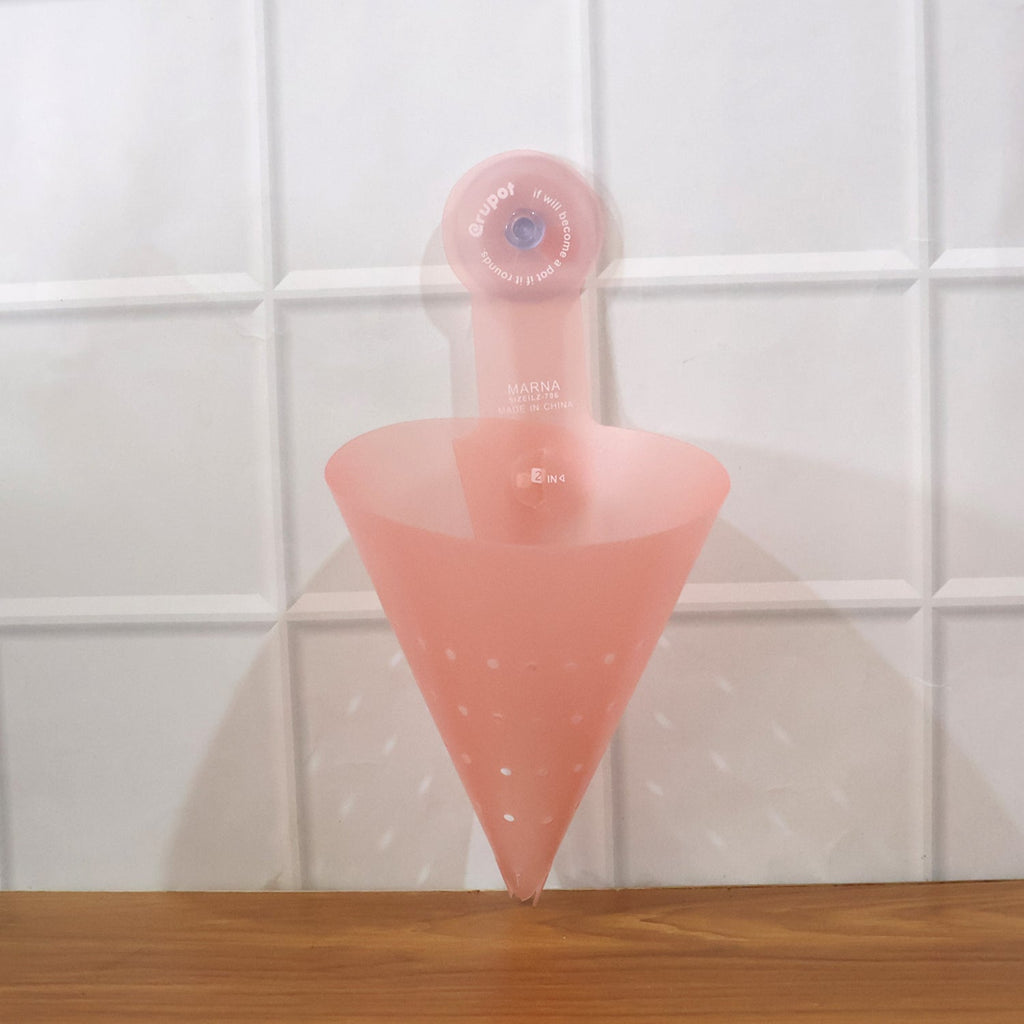 A pink silicone sink strainer with a suction cup, empty, attached to a white tiled wall above a wooden surface.