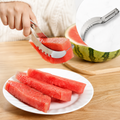 A hand uses a stainless steel watermelon slicer to lift a slice of red watermelon from a larger fruit.