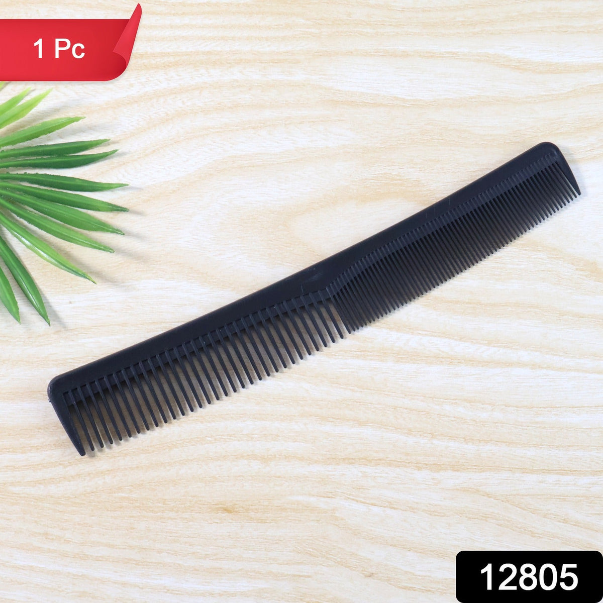 A single black dual-tooth comb lies on a light wooden surface next to a green leaf.
