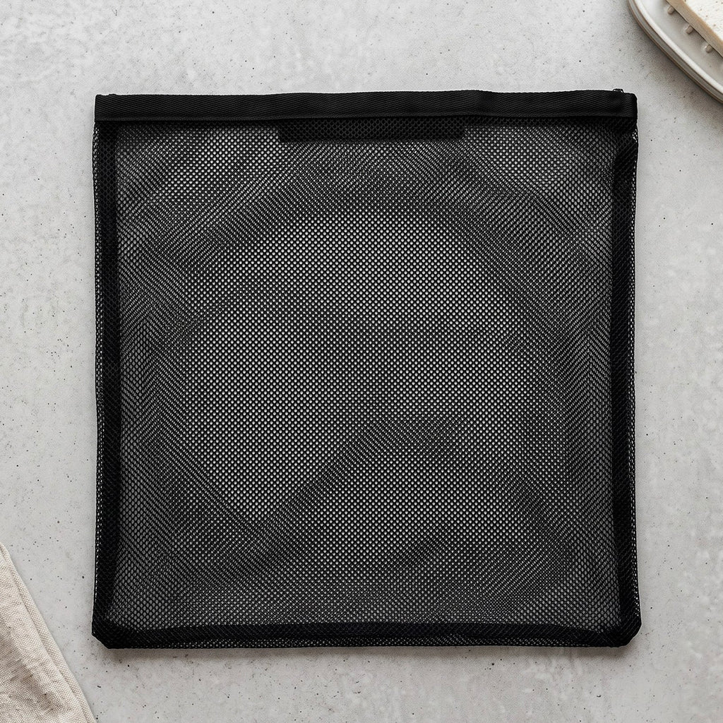 A flat black mesh zipper storage bag is laid out on a light grey textured surface.