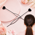 Two black heart-shaped hair styling tools on a pink surface, with one shown in use on a ponytail.