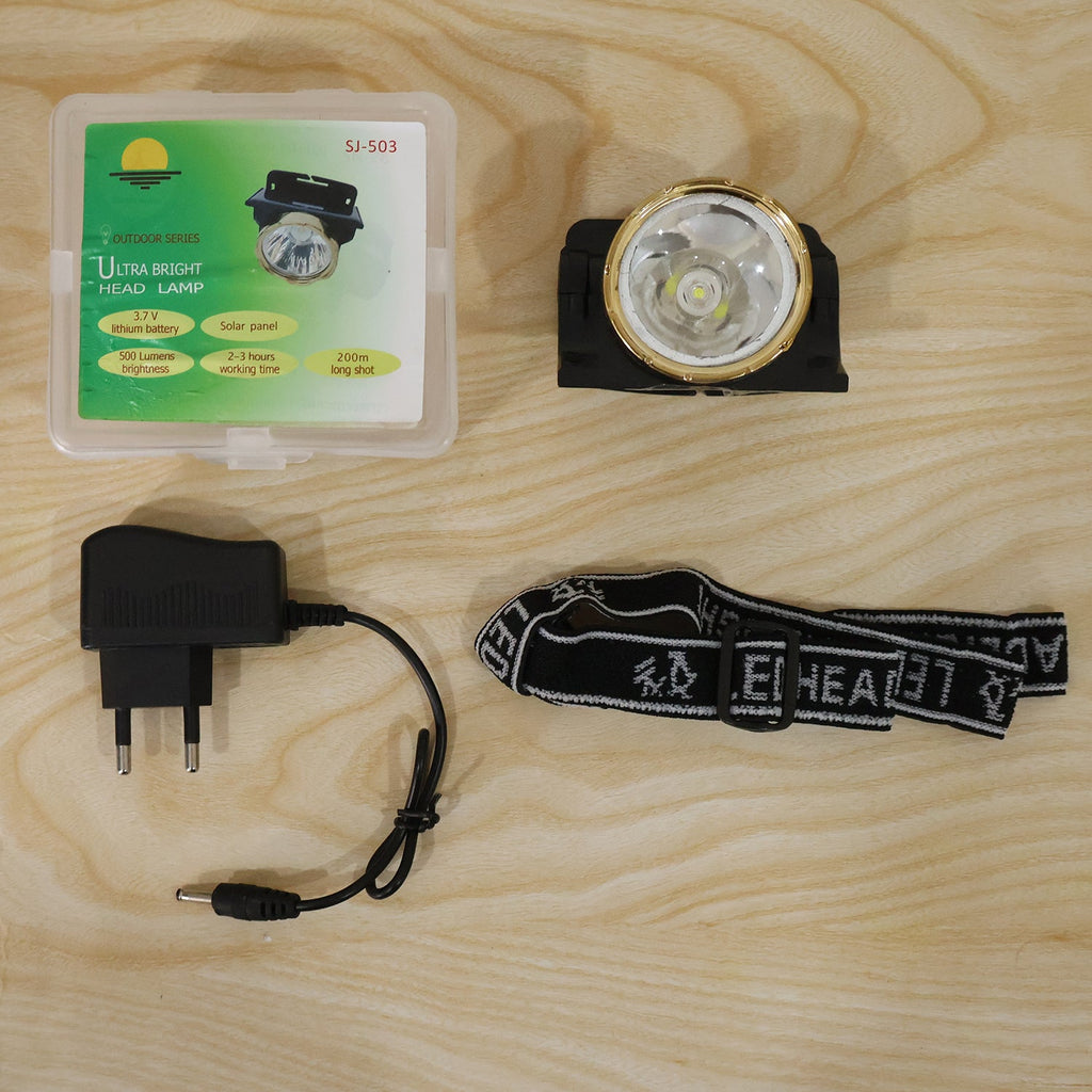 A black and gold headlamp, a charger, a head strap, and a clear box with product information on a light wooden surface.