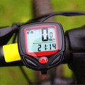 Close-up of a black and red bicycle computer displaying 0 KM/hr and 21:14 on a bike handlebar.