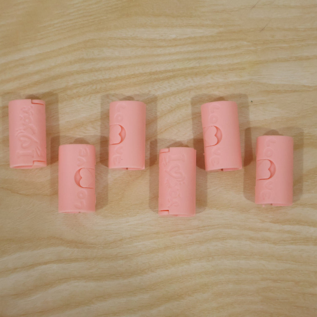Six pink plastic bed sheet clips with a 'Love' design are arranged on a light wooden surface.