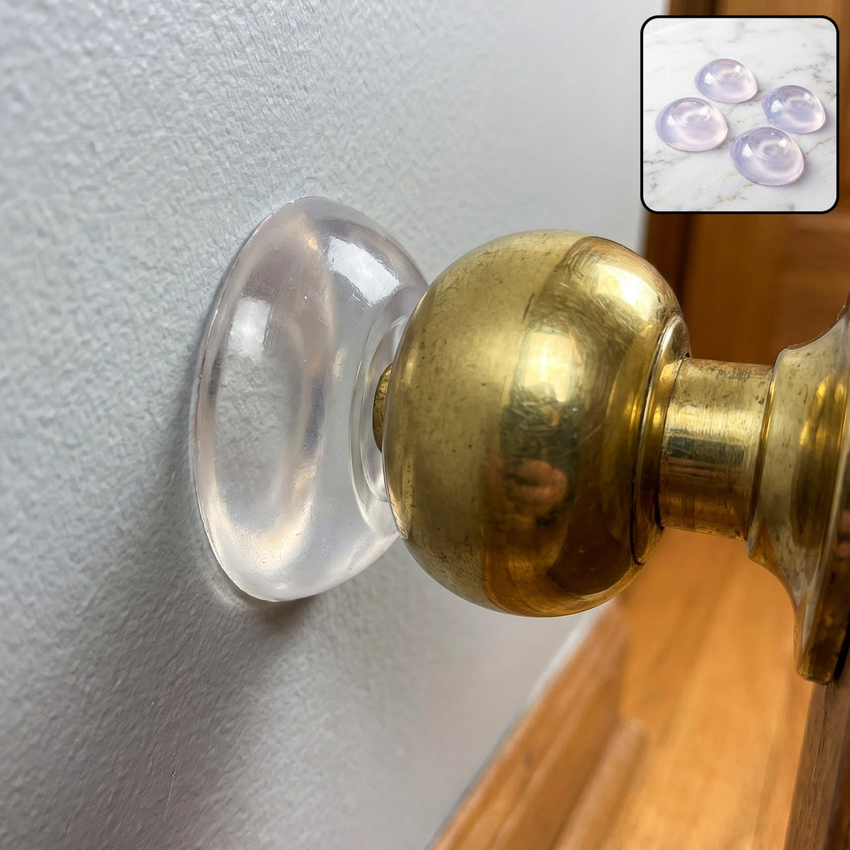 A clear silicone bumper adhered to a light gray wall, protecting it from a brass doorknob.