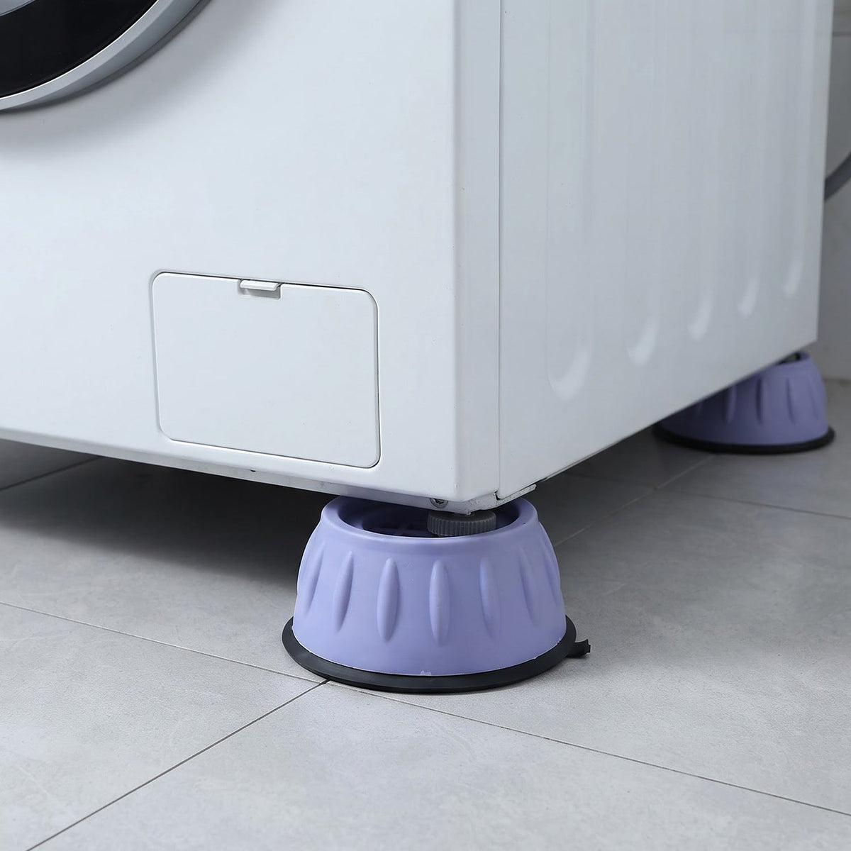 Two purple anti-vibration pads supporting the front and back corners of a white washing machine on a tiled floor.
