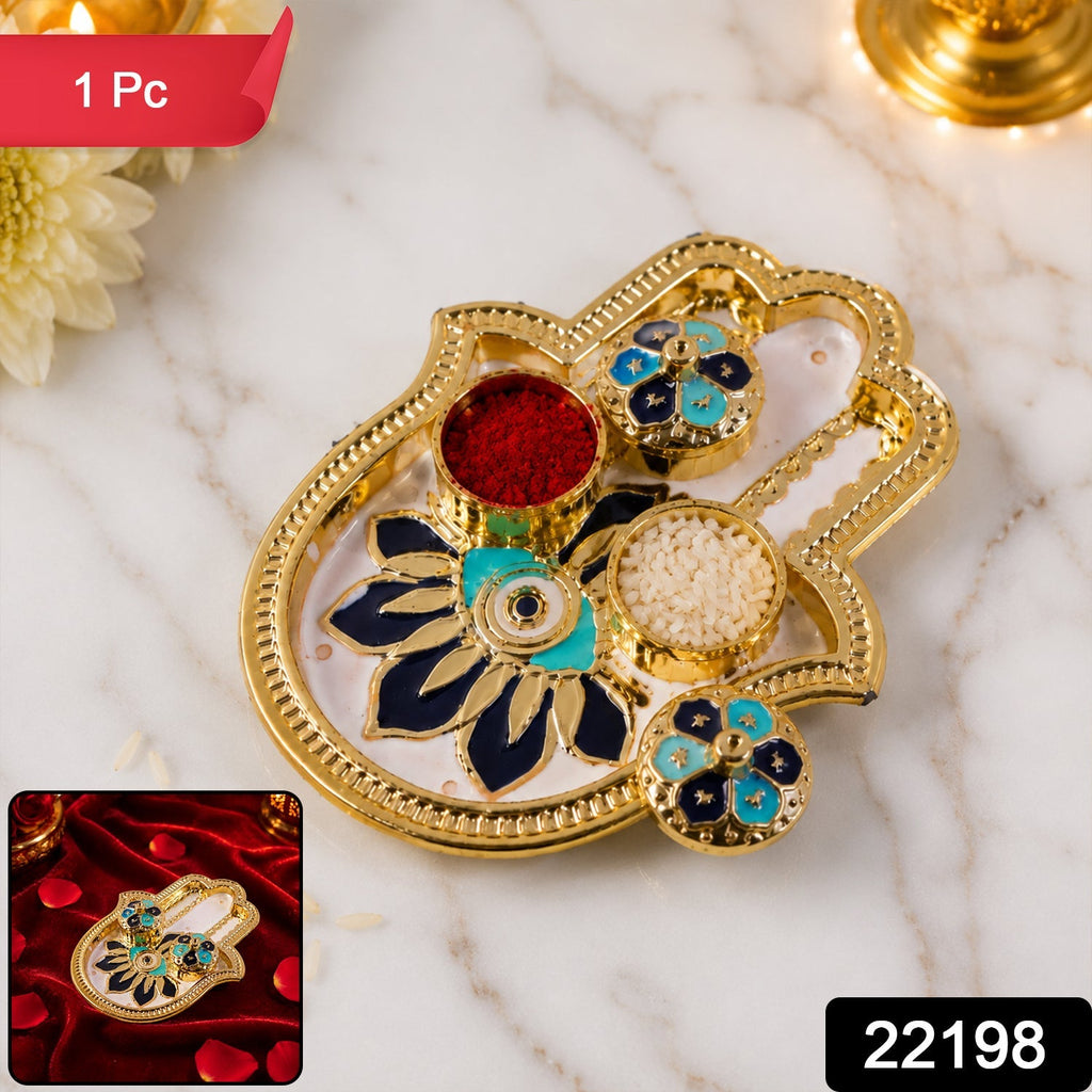 Golden hamsa hand thali with red kumkum, white rice, and blue and black enamel floral designs.