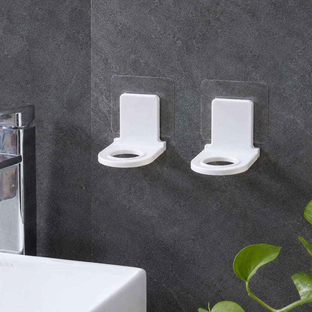 Two white plastic bottle holders with clear adhesive pads lying on a light gray tiled floor beside a white bathtub.