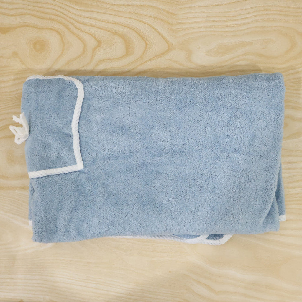 Folded light blue bath towel wrap with white trim and a small pocket, laid on a light wooden surface.