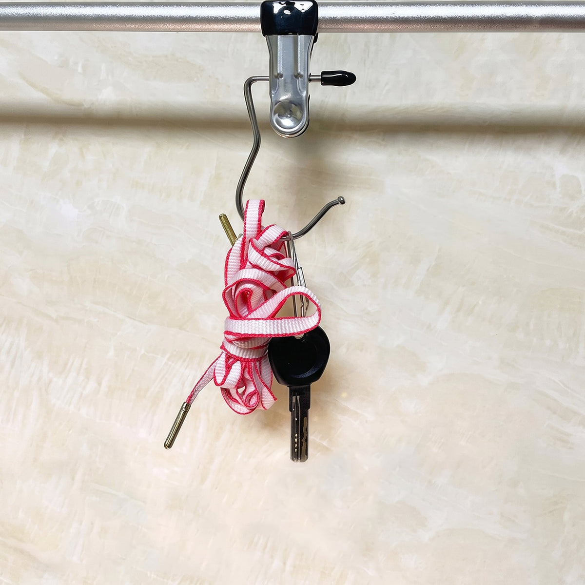 A close-up of a single metal clip hanger with a black rubber tip hangs from a silver rod, holding a coiled pink and white