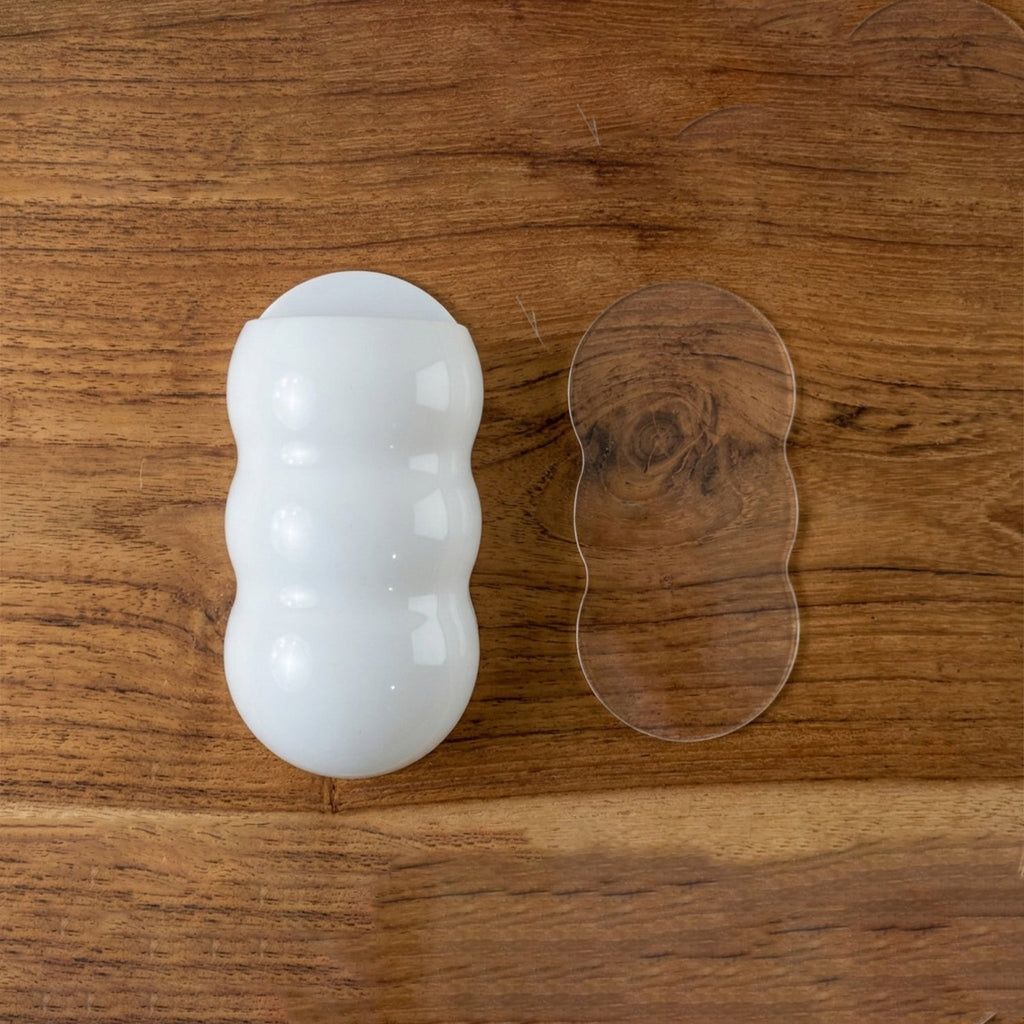 White, caterpillar-shaped holder and a clear adhesive strip on a light brown wooden surface.