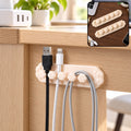 Beige flower-shaped cable organizer clip with five slots holding black, white, and grey cables under a wooden desk.