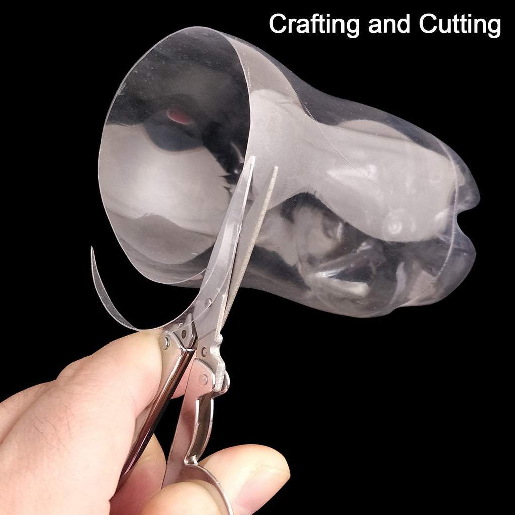 A hand uses open silver folding scissors to cut a clear plastic bottle against a black background.