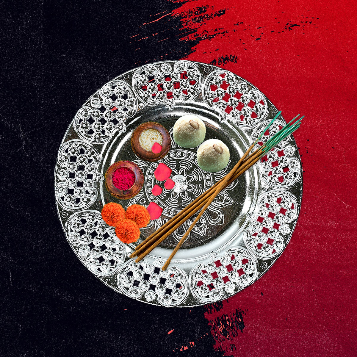 A silver-colored plastic pooja thali filled with sweets, incense sticks, and flower petals on a red and black textured