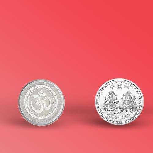 Two silver coins, one with Om and one with Lakshmi and Ganesha, displayed side-by-side on a red background.