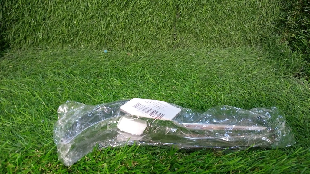 A clear plastic-wrapped stainless steel watermelon slicer with a white label lies on a vibrant green grassy surface.