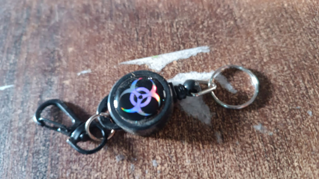 A black retractable keychain with a biohazard symbol resting on a wooden surface.